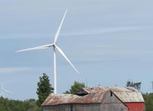 Wind turbine behind red barn with dilapidated roof 